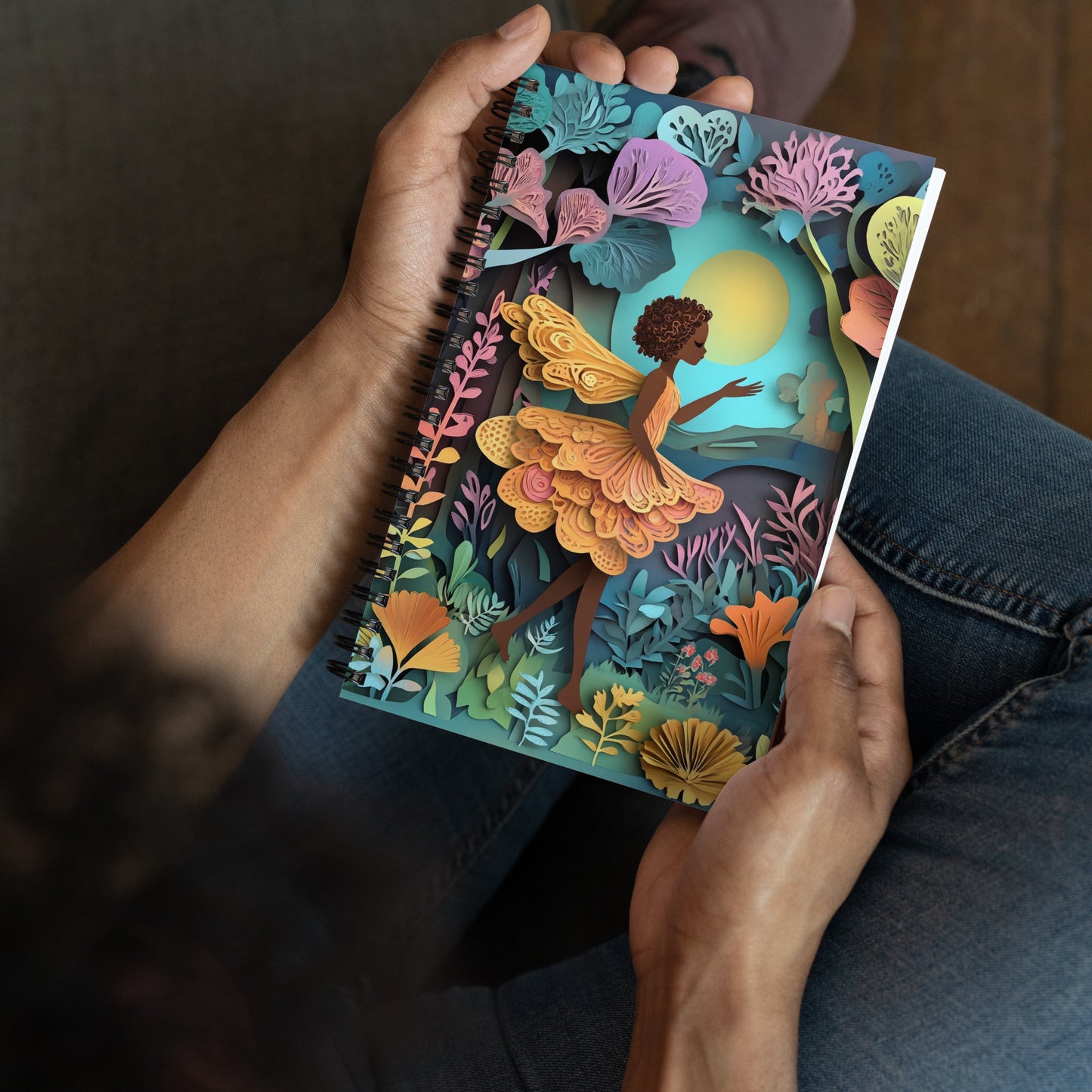 Handheld perspective view of a notebook with a fairy in a garden.