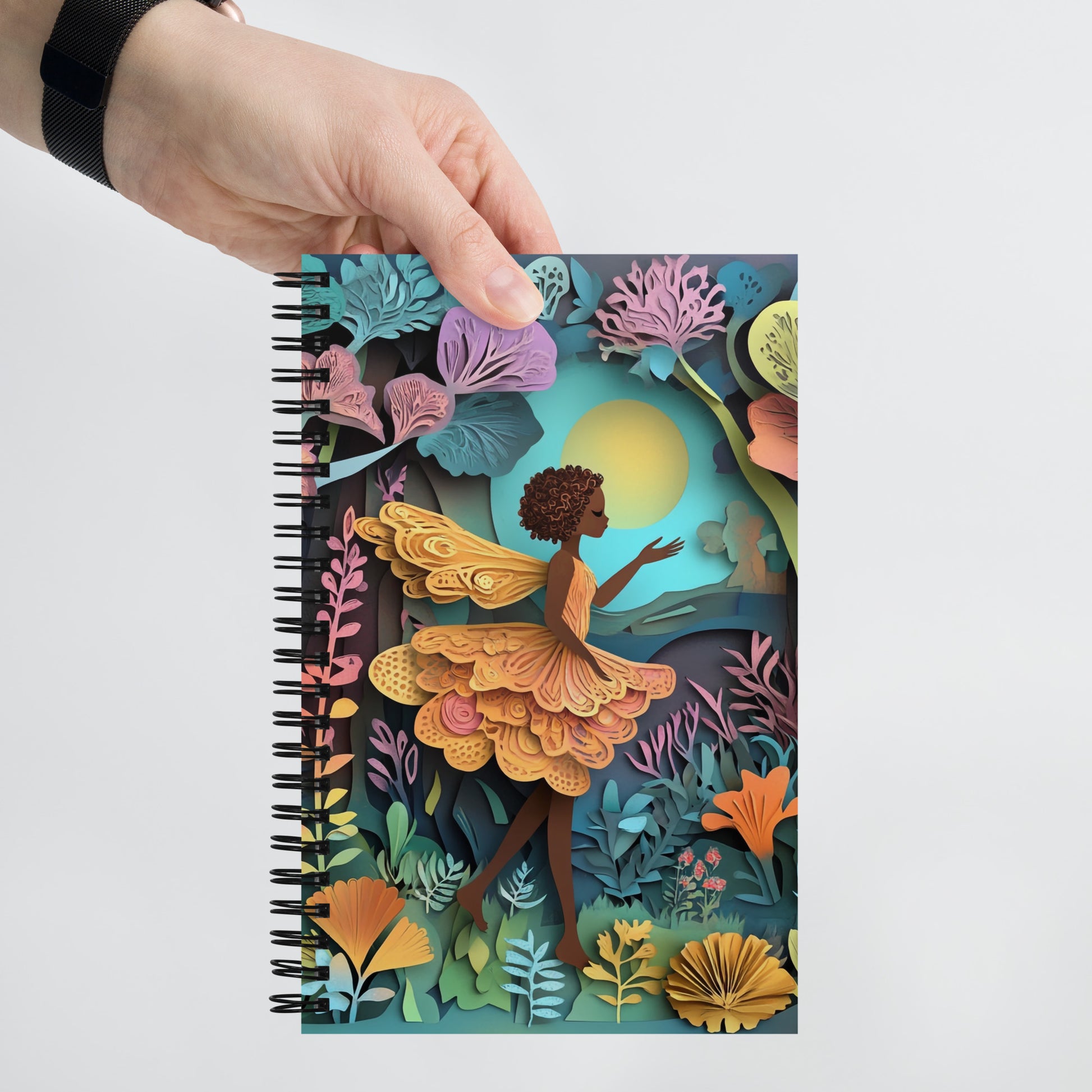 Handheld view of a  notebook with a fairy in a garden.