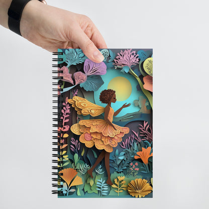Handheld view of a  notebook with a fairy in a garden.